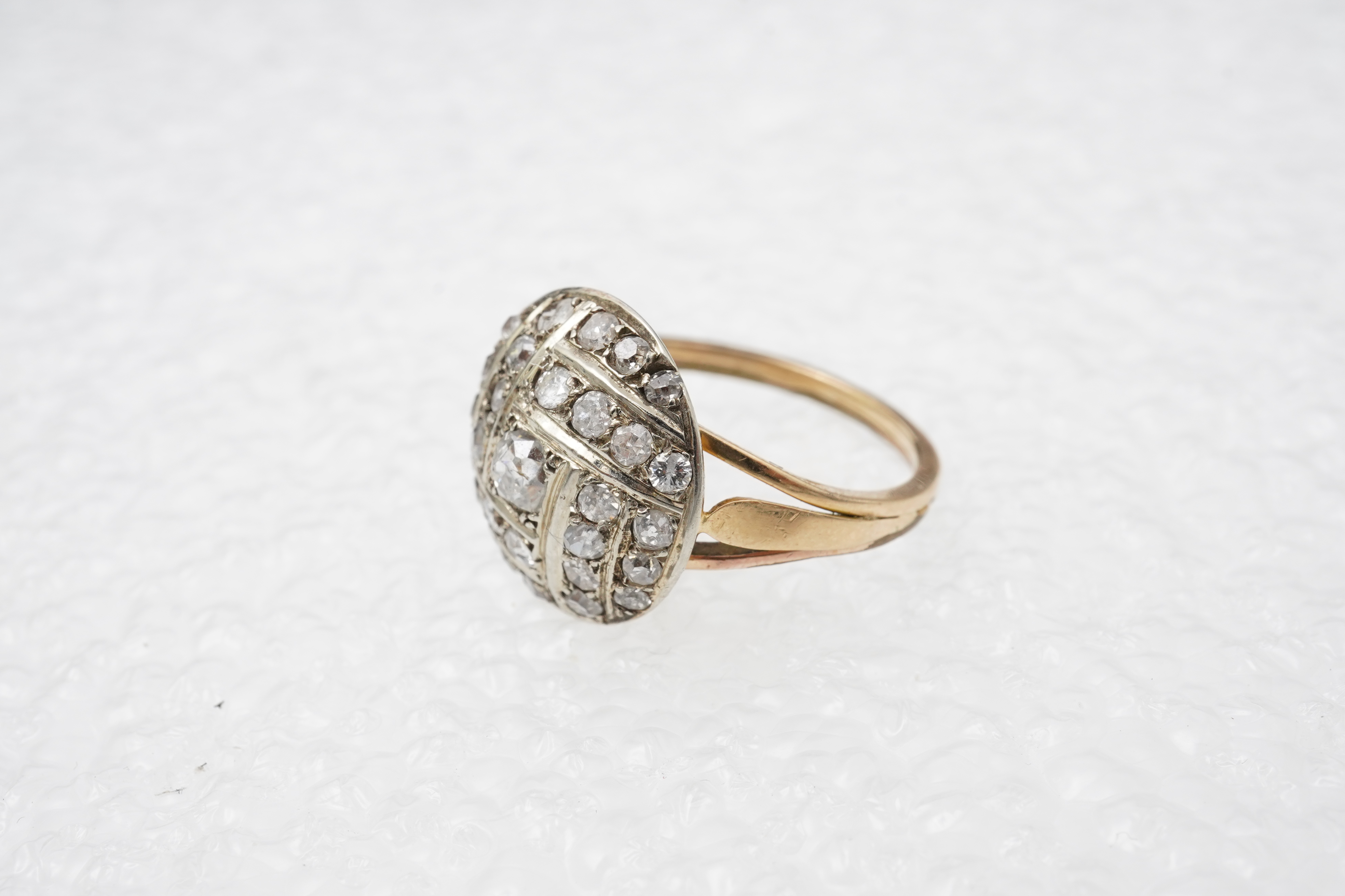A diamond ring, centring on a circular motif of bombé design, set with geometric arrangements of cushion-shaped, single- and circular-cut diamonds totalling approximately 0.90 carats, to a gold band, size M1/2, indistinc